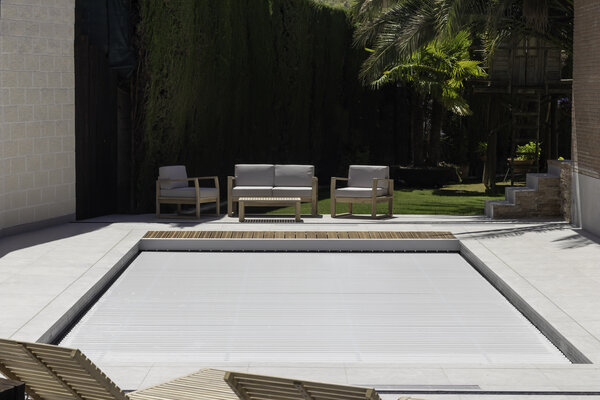 Ein moderner Swimmingpool mit geschlossener Rollschutzabdeckung und Sitzmöbeln im Hintergrund.